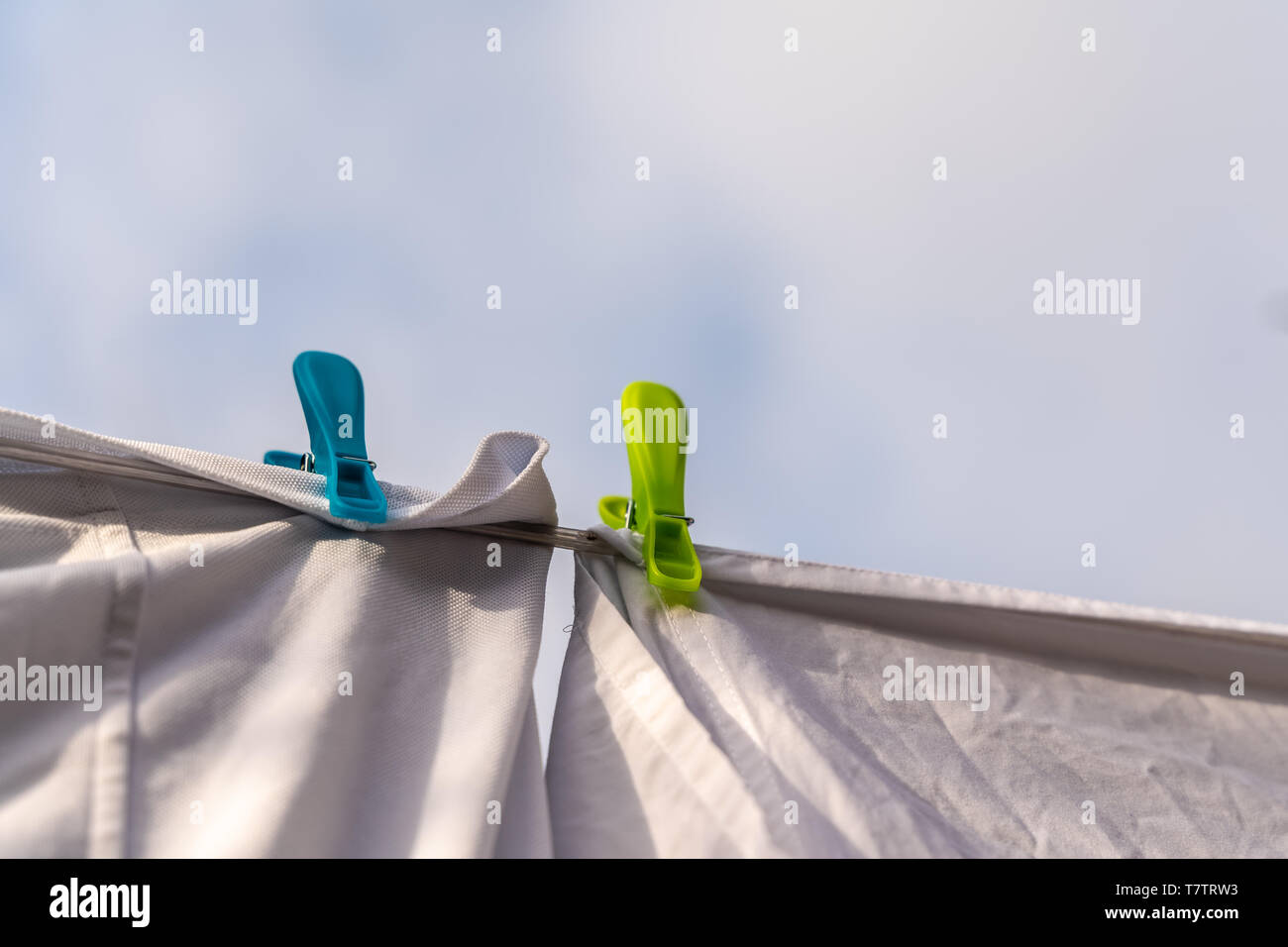 White clothes hung out to dry on a washing line and fastened by the clothes pegs against the blue sky in the bright warm sunny day Stock Photo