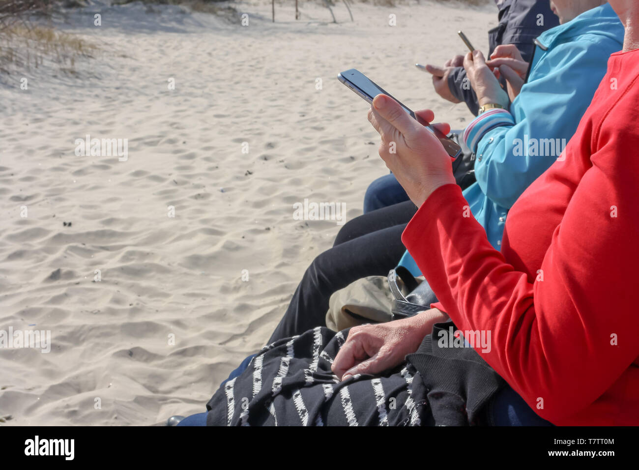 Elderly persons sitting on a bench at the seaside and use smartphones Stock Photo