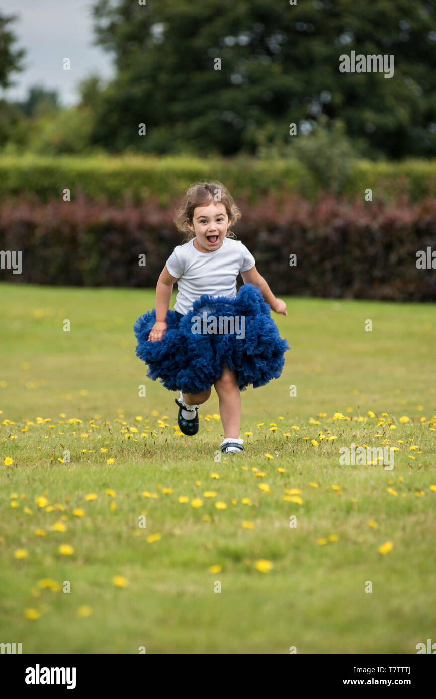 young girl running through a field wearing a white t-shirt and blue skirt Stock Photo