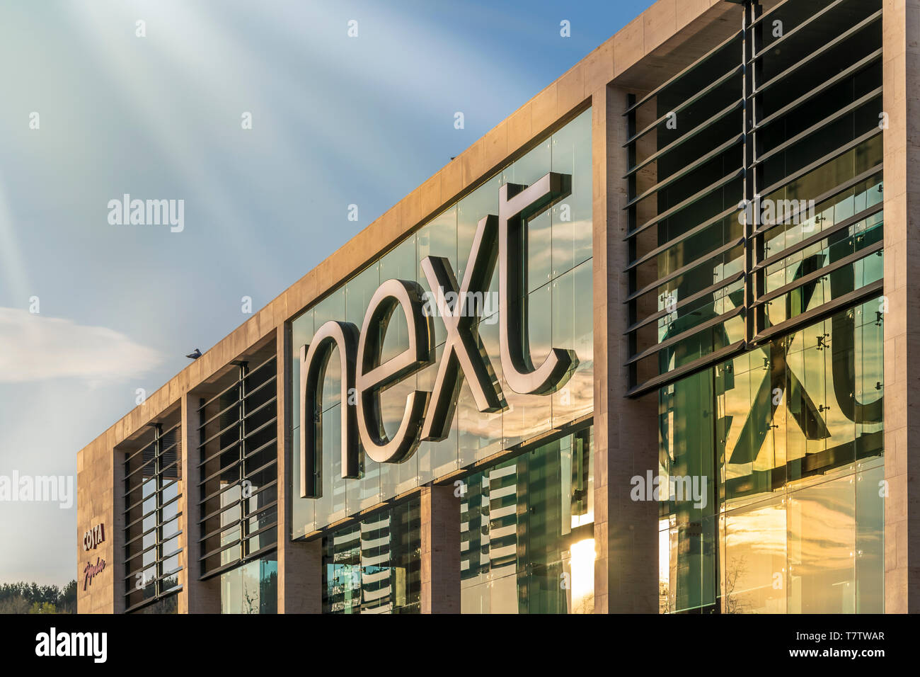 The late afternoon sun lights up the modern glass storefront of Next Retail in Plymouth, Devon. Stock Photo