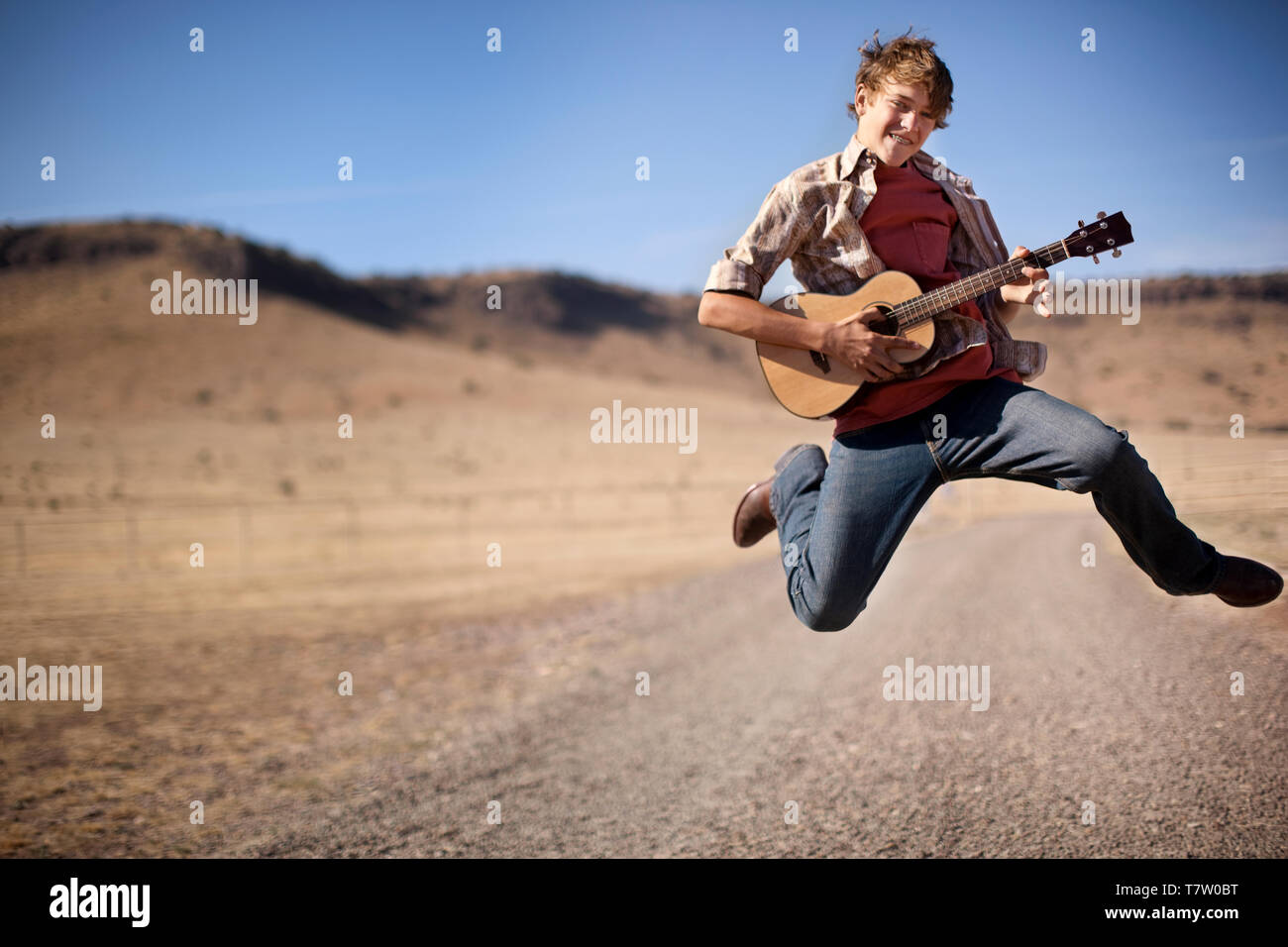 Smiling teenage boy jumping in the air while playing an acoustic guitar