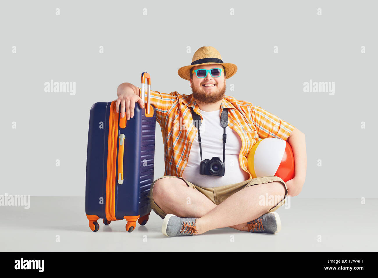 Fat funny man with a suitcase smiling on a gray background. Stock Photo
