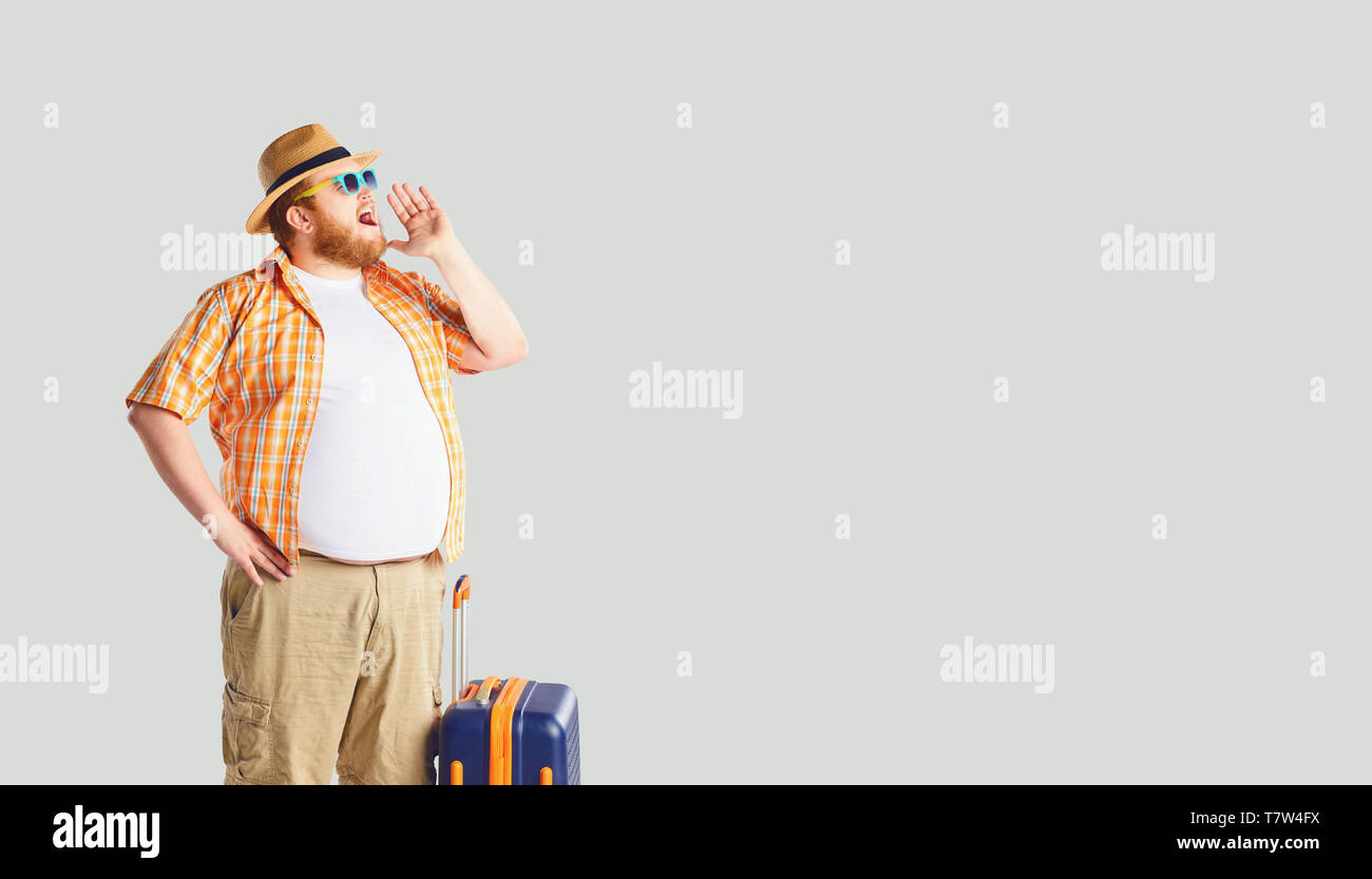 Fat funny man with a suitcase screaming on a gray background. Stock Photo