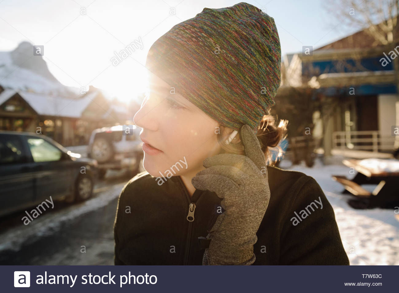 Teenage girl runner adjusting headphones on sunny, snowy sidewalk Stock Photo