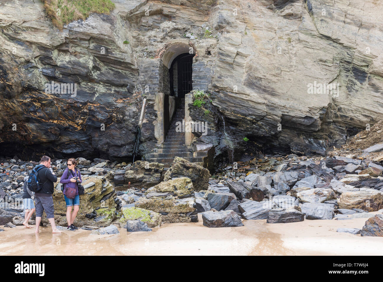 Holidaymakers exploring the rocks around the historic disused entrance to the tunnel leading from Great Western Beach to the Hiotel Victoria in Newqua Stock Photo