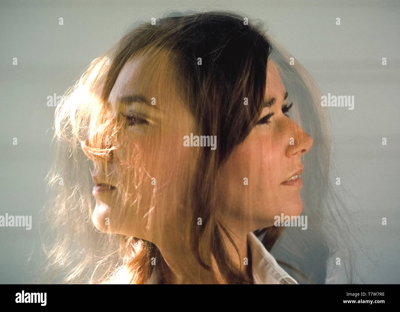 Overlapping images of the same face show the creativity that can be achieved with a camera. This double-exposure photograph of the face of a pretty woman was made with natural sunlight against a plain background. She turned her head to the left for a profile with the first exposure, and then turned it to the right for a profile of the opposite side of her face with another exposure on the same frame of film. Sunlight falling directly on her from the left highlighted some strands of hair in the first exposure and some of her face in the second exposure. Stock Photo