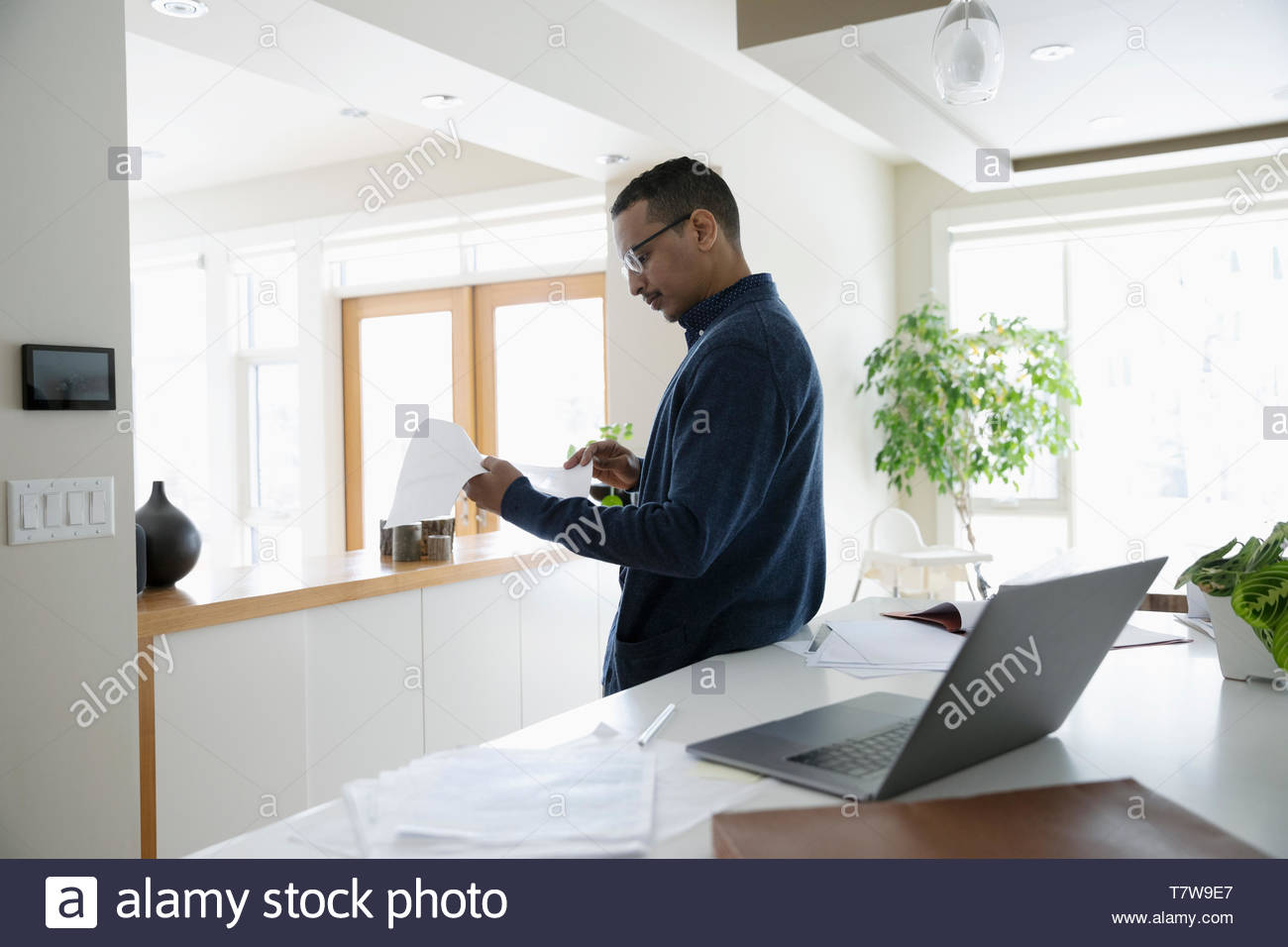 Man working from home, reviewing paperwork in kitchen Stock Photo