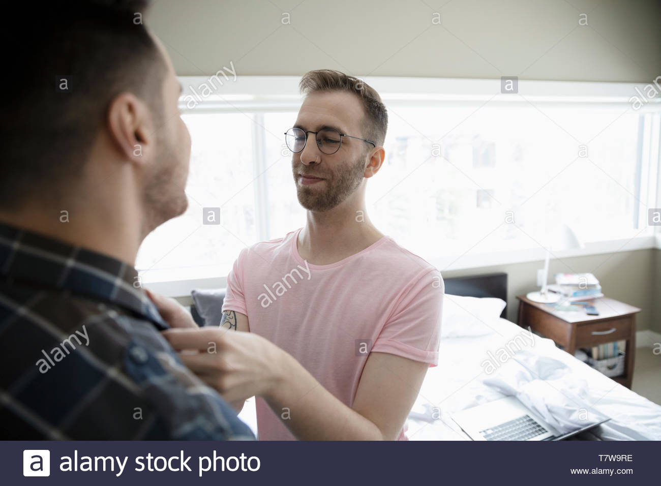 Gay man helping boyfriend get dressed in bedroom Stock Photo