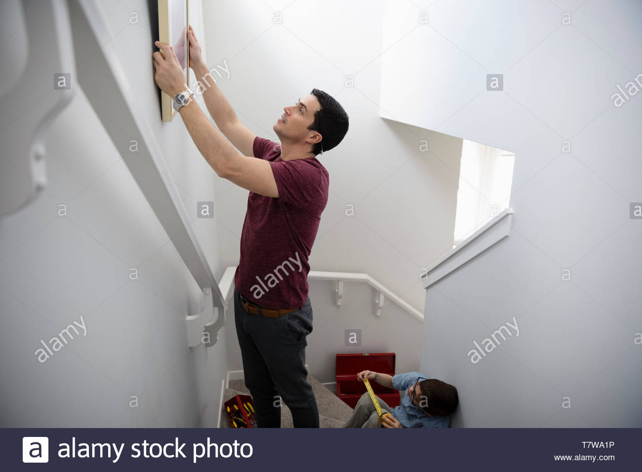 Man hanging picture frame on wall above stairs Stock Photo Alamy