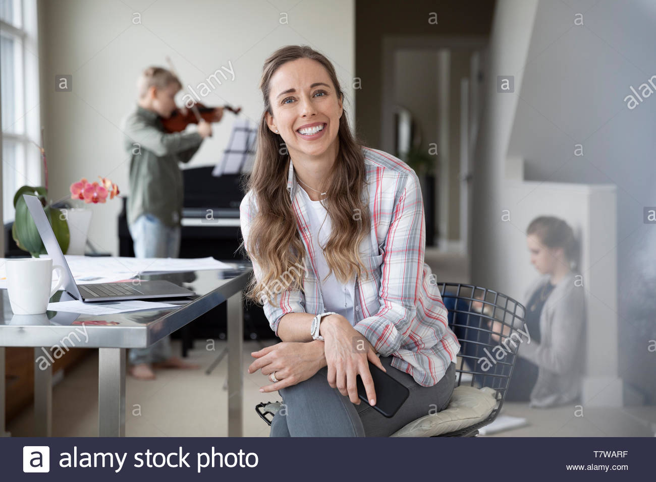 Portrait confident, happy mother working from home while children do homework and practice violin in background Stock Photo