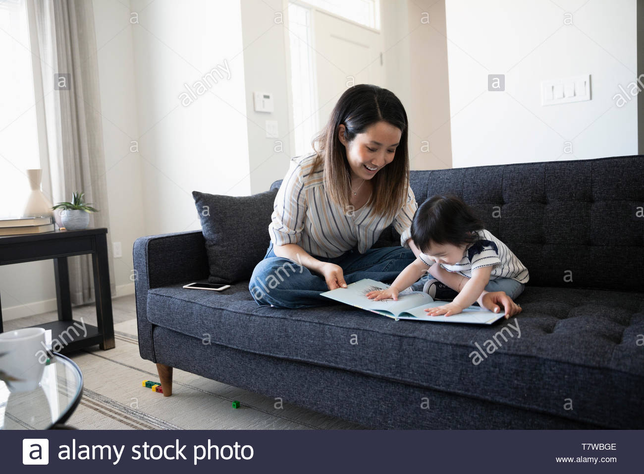 Mother and toddler daughter reading book on living room sofa Stock Photo