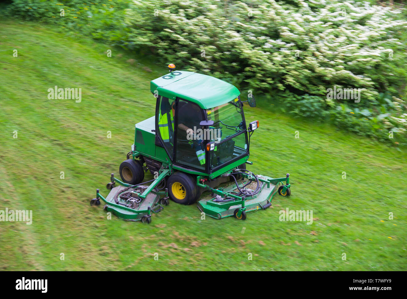 A riding commercial landscaper of a community or city services on the big lawn mower cutting the grass Stock Photo