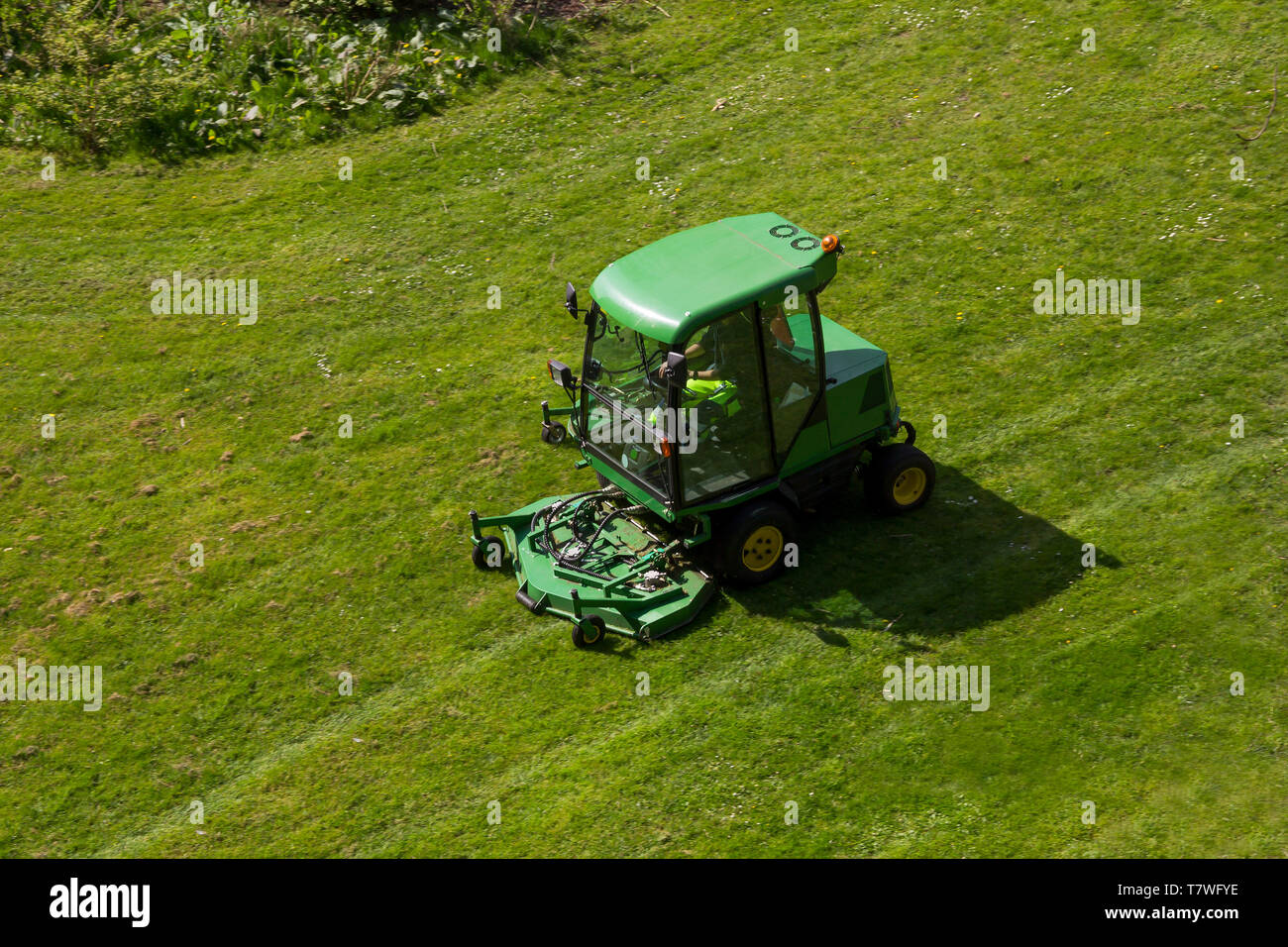 A riding commercial landscaper of a community or city services on the big lawn mower cutting the grass Stock Photo