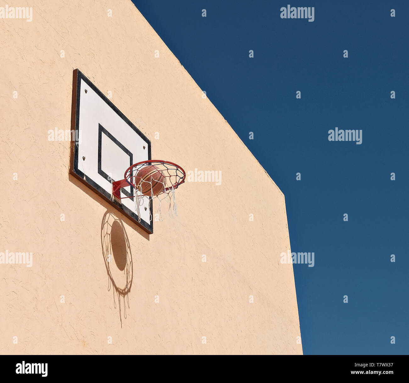 basketball in basketball hoop against yellow wall. The ball and net create a shadow on the wall. Stock Photo