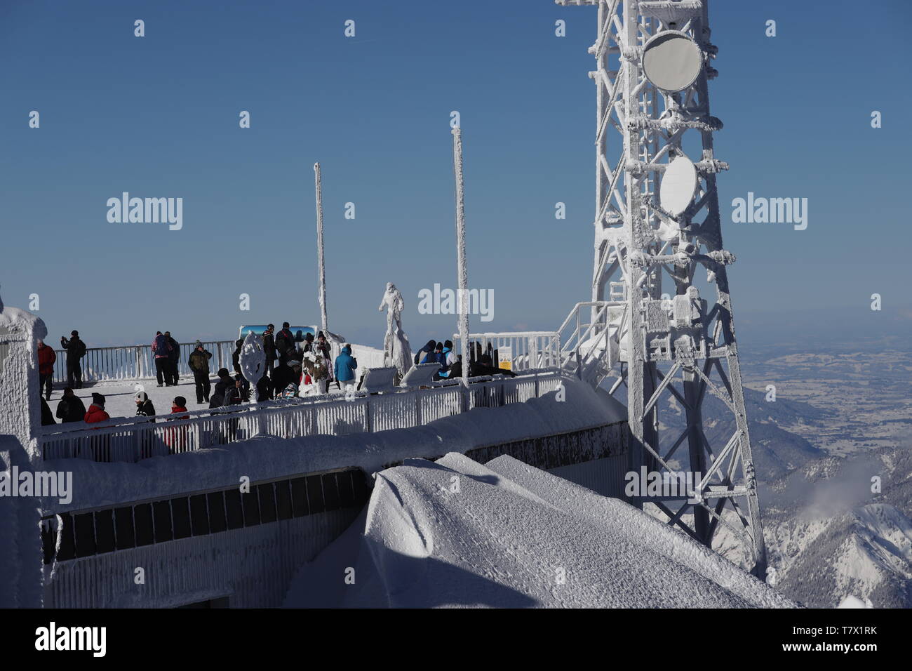Zugspitze:: Blick auf die winterliche österreichische Plattform mit Besuchern und der vereisten hölzernen Statue 'Himmelsstürmer'. Stock Photo