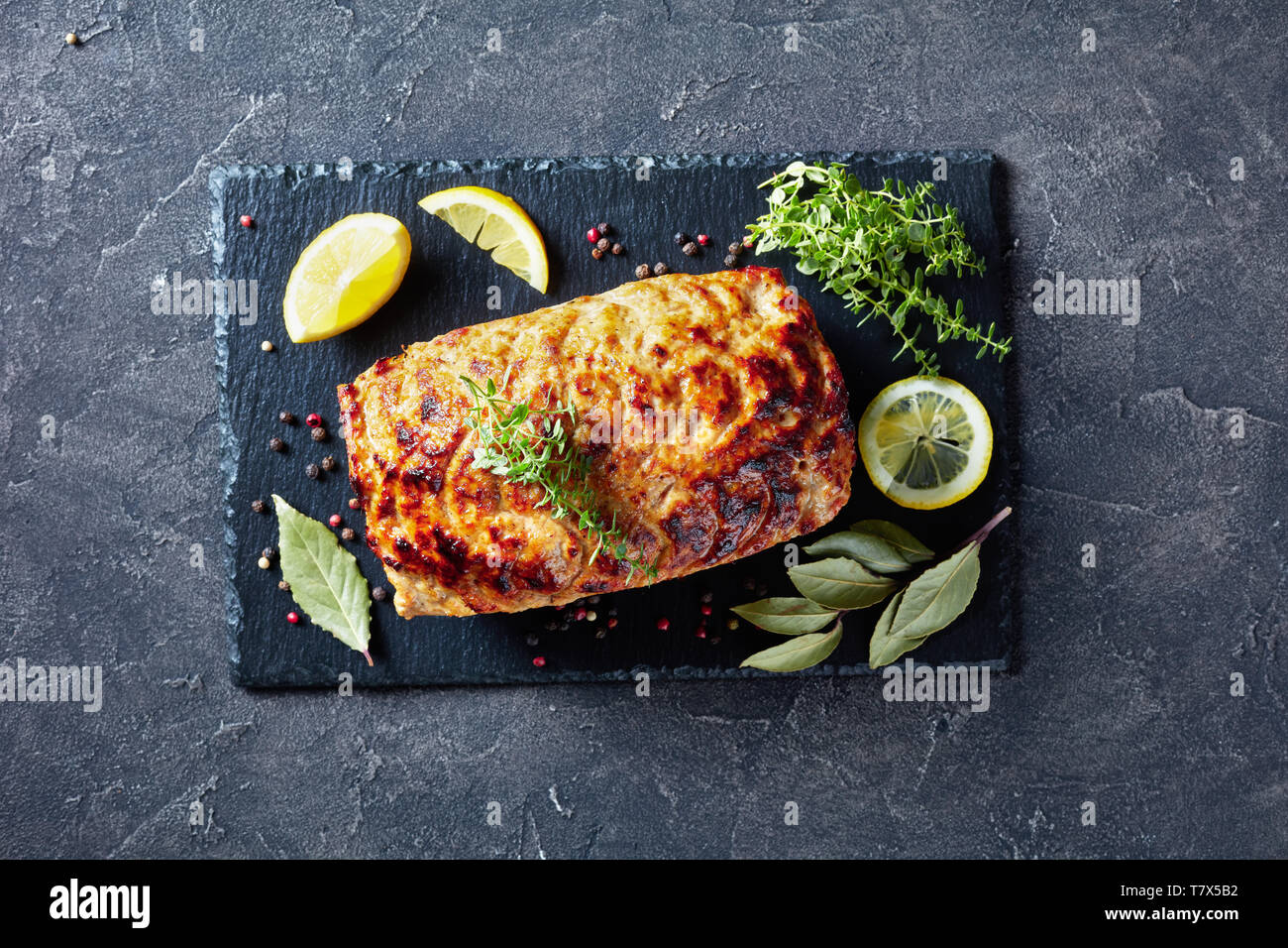 baked chicken meatloaf terrine on a slate flat plate with lemon slices and fresh thyme on a