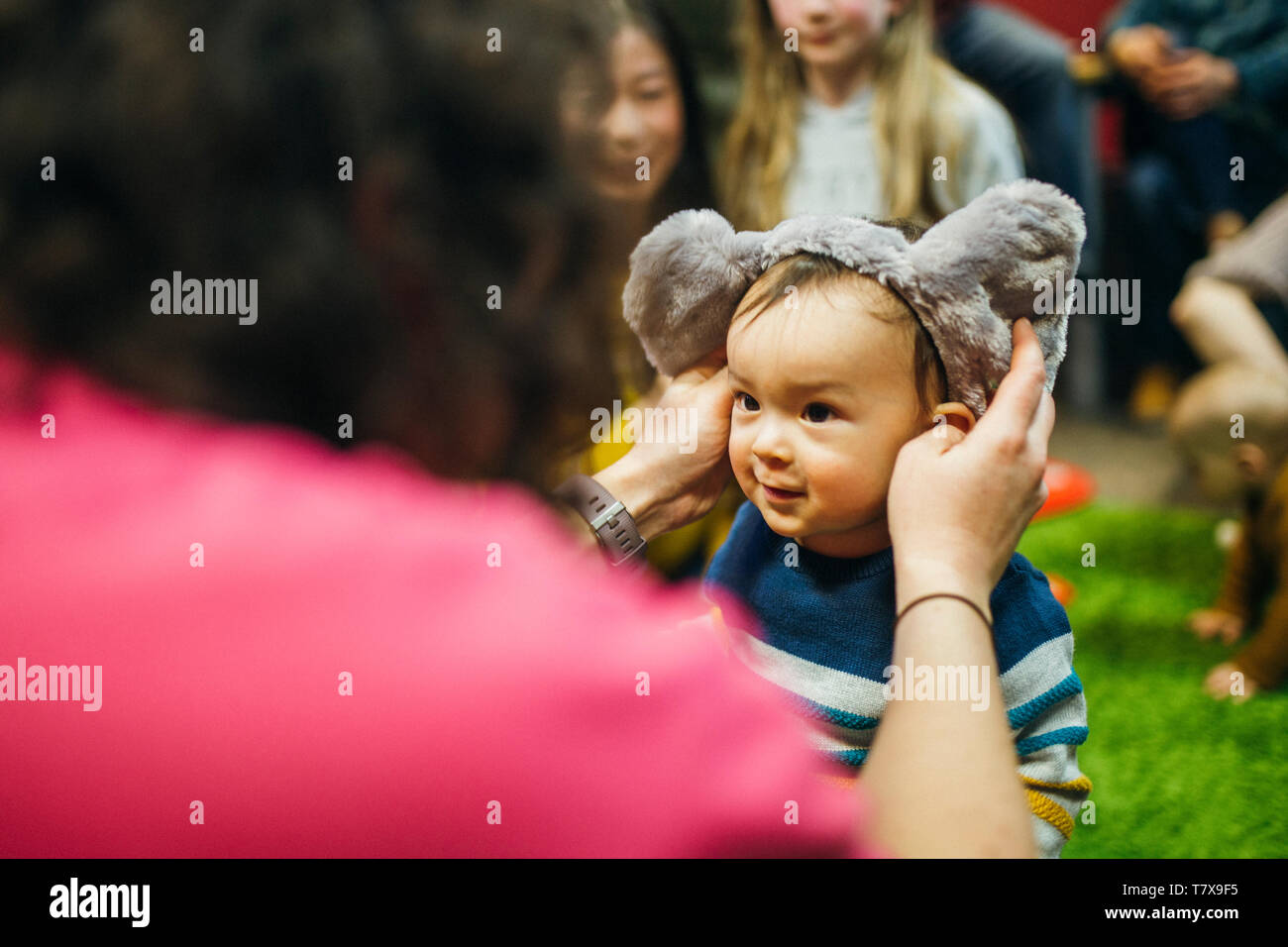 Little boy is playing with his mother in a preschool group. She is putting a headpiece on him. Stock Photo