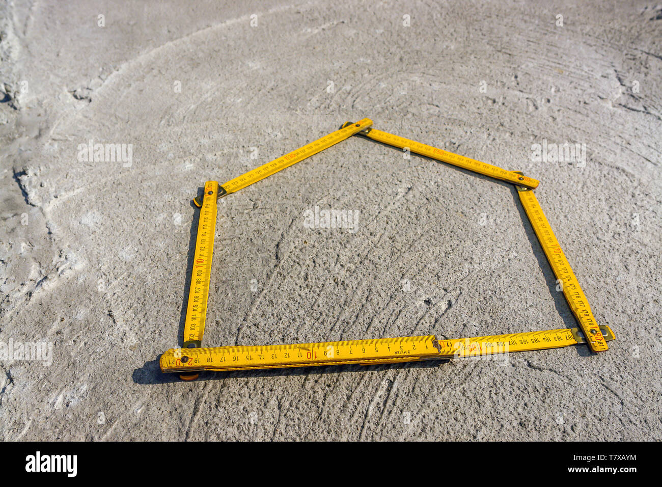House-shaped yellow wooden folding ruler placed on concrete foundation surface Stock Photo