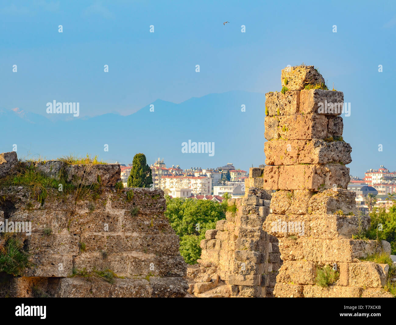 The ruins of an ancient city close up on the background of the modern town and mountains. Concept of destruction and rebirth Stock Photo