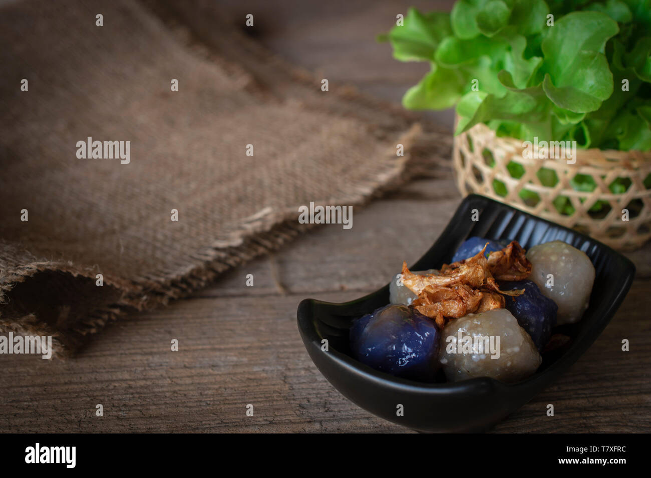 Sago pork in black plate with fried garlic toping have Sack place left hand and lettuce basket place backside on wood background Stock Photo