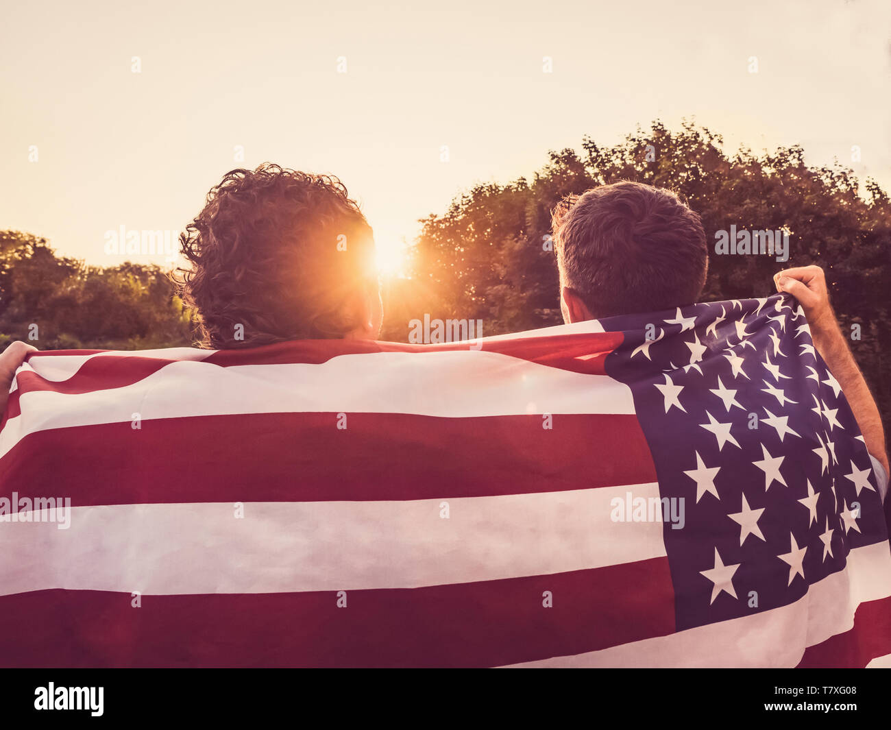 Two friends hold American Flag at sunset Stock Photo - Alamy