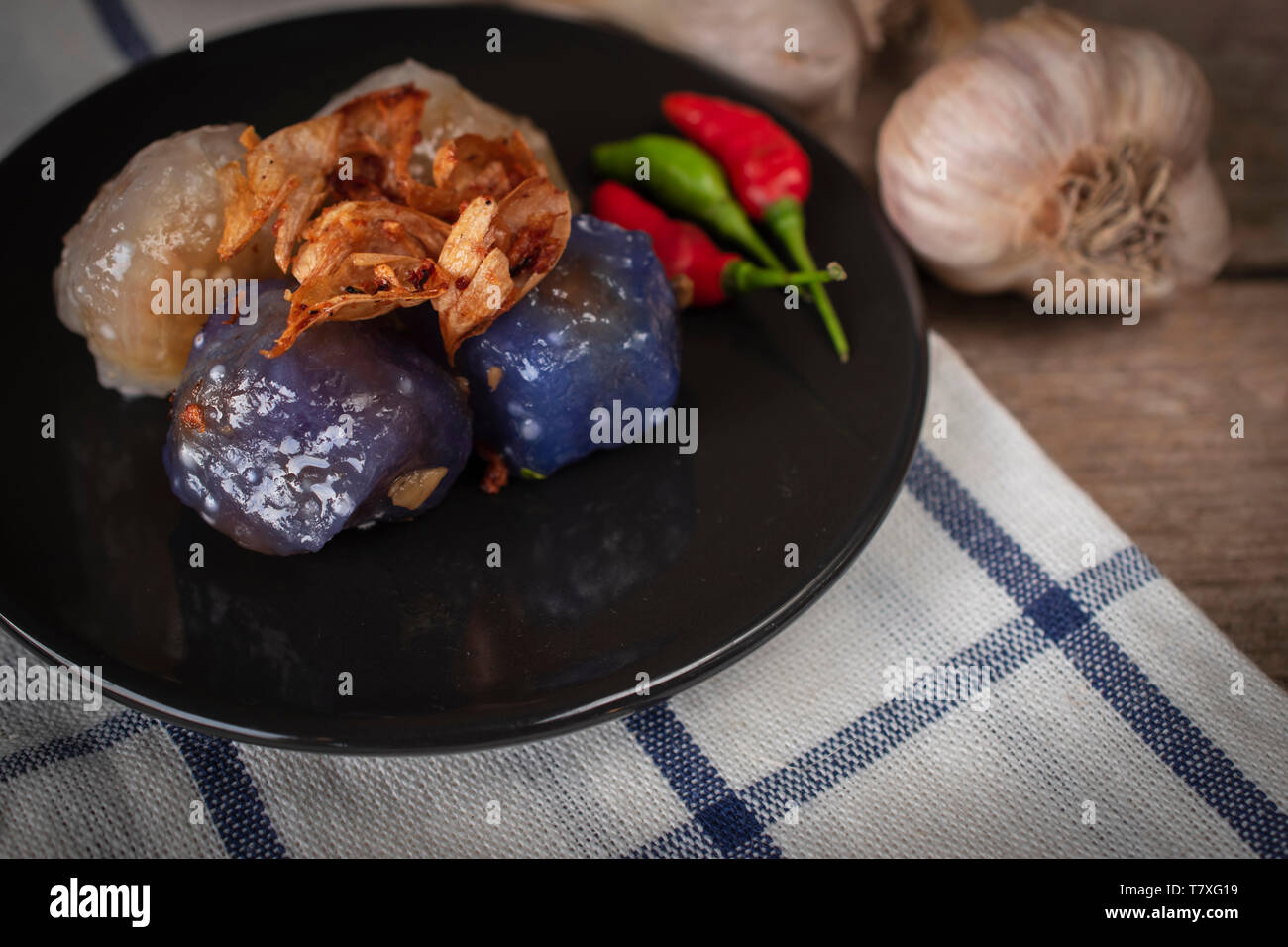 Sago pork in circle black plate with fried garlic toping have garlic place backside and chilli place on black plate on tablecloth and wood background Stock Photo