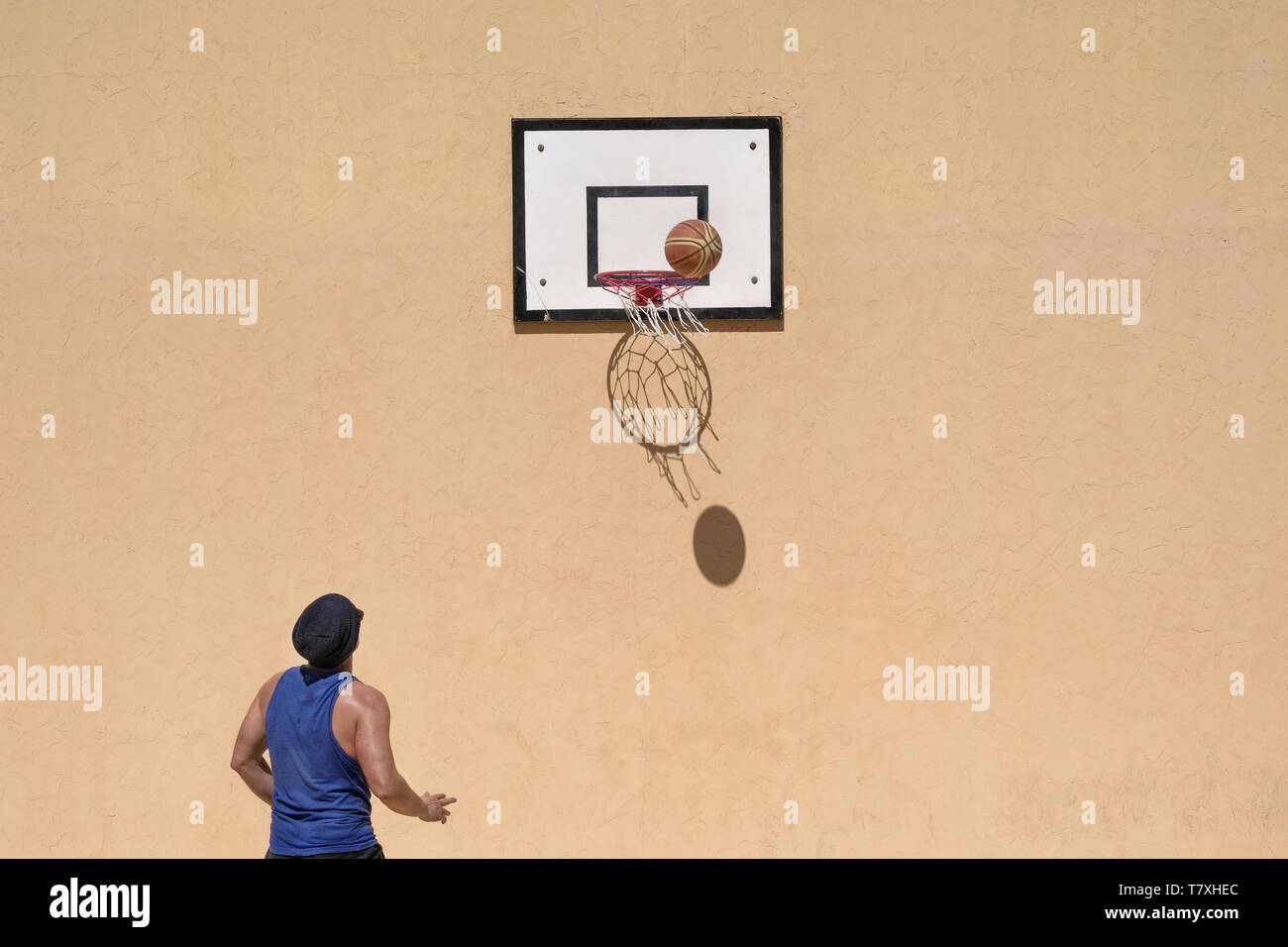 one man is playing basketball on his own in bright sunshine and the basketball creates a shadow on the yellow wall Stock Photo