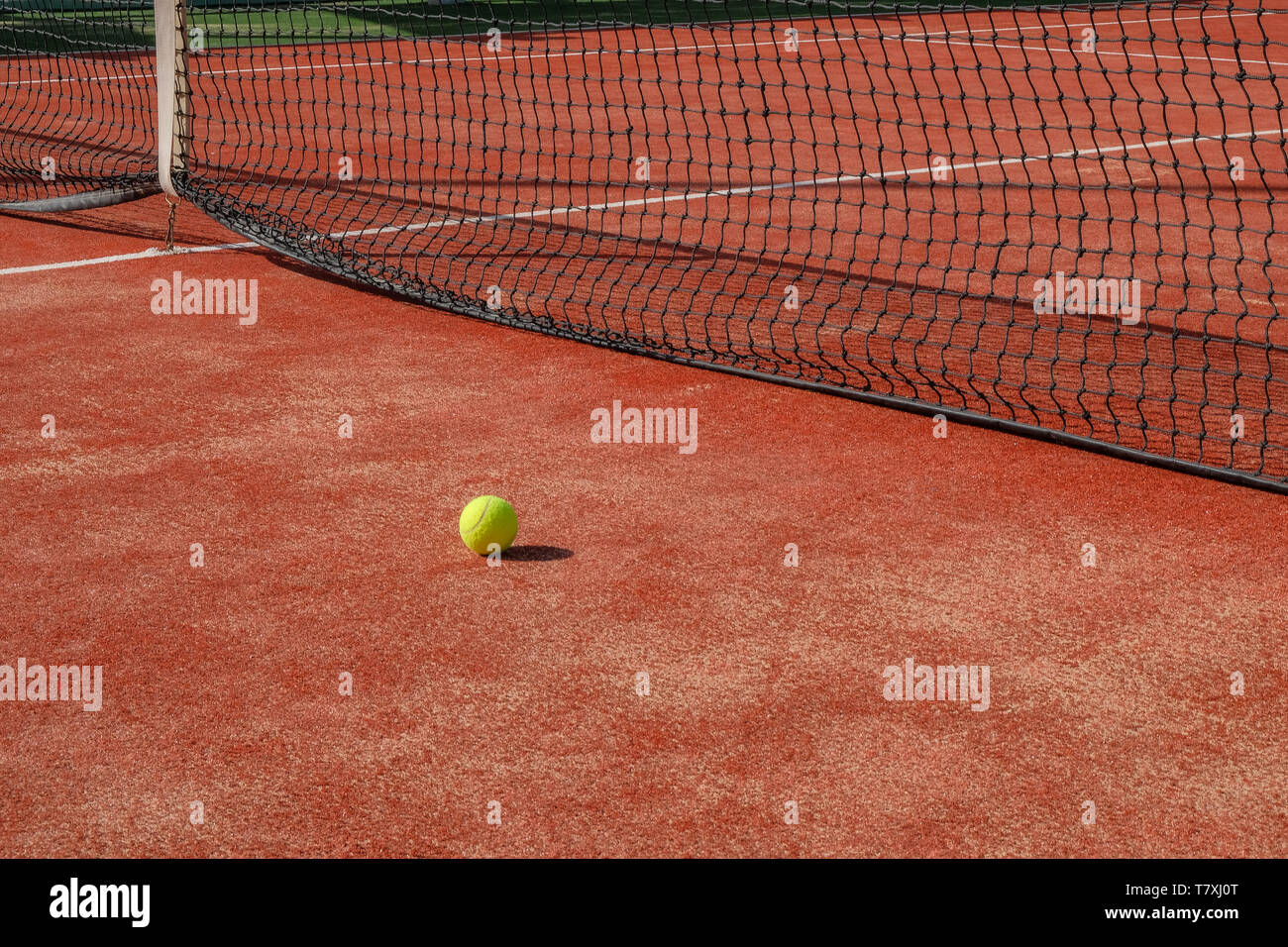 one tennis ball lying in front of a tennis net on a tennis court Stock Photo