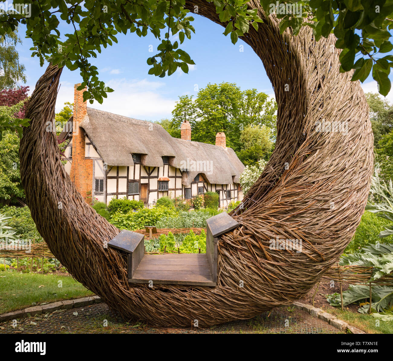 Stratford-upon-Avon, Warwickshire / UK - June 18th 2018: Anne Hathaway's half-timbered cottage and its garden framed by a circular willow seat. Stock Photo