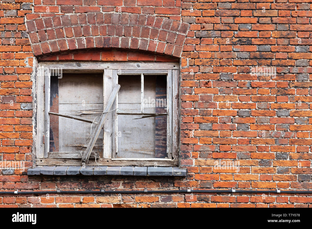Old locked window with broken wooden frame in grungy brick wall