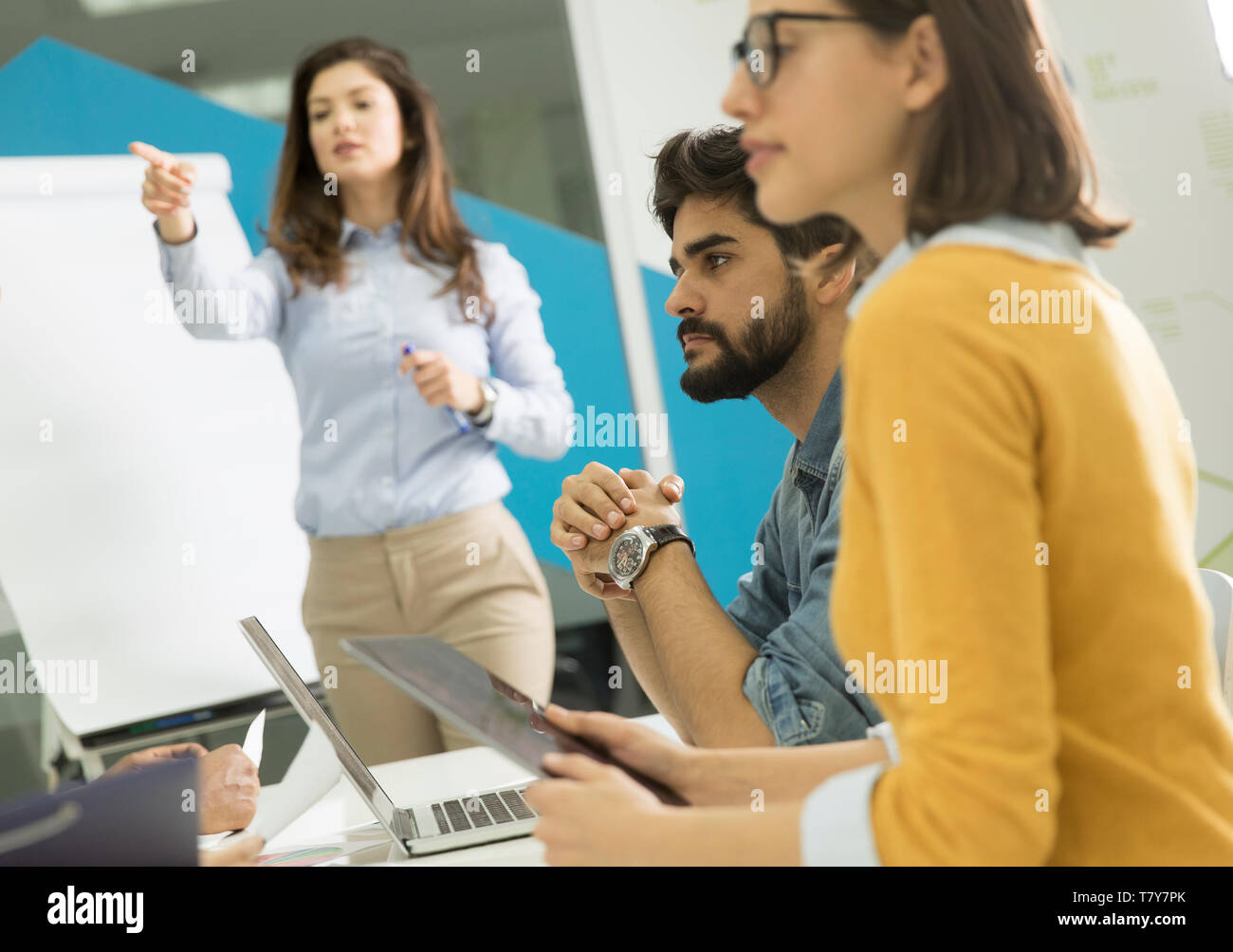 Confident young team leader giving a presentation to a group of young colleagues as they sit grouped by the flip chart in the small startup office Stock Photo