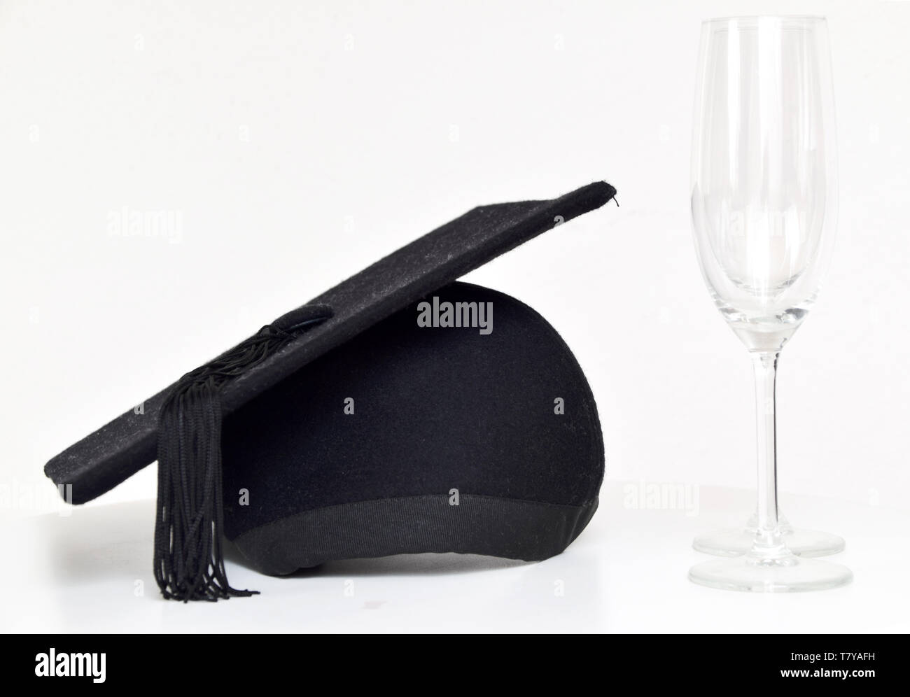 Graduation cap and champagne glasses on table with a white wall in the