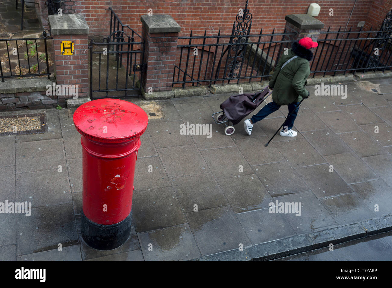 Looking down from the top of a London bus on to the top of a Royal Mail postal box as a lady wearing a red hat walks along the Walworth Road in Southwark, on 9th May 2019, in London, England. Stock Photo