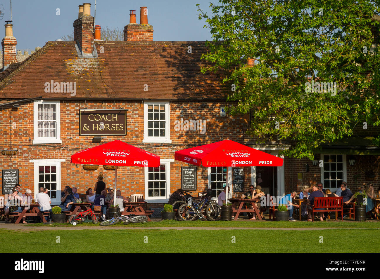 People relax in the evening sun under bright red sunshades outside the Coach and Horses pub by the Kinecroft, Wallingford by a Horse Chestnut tree Stock Photo
