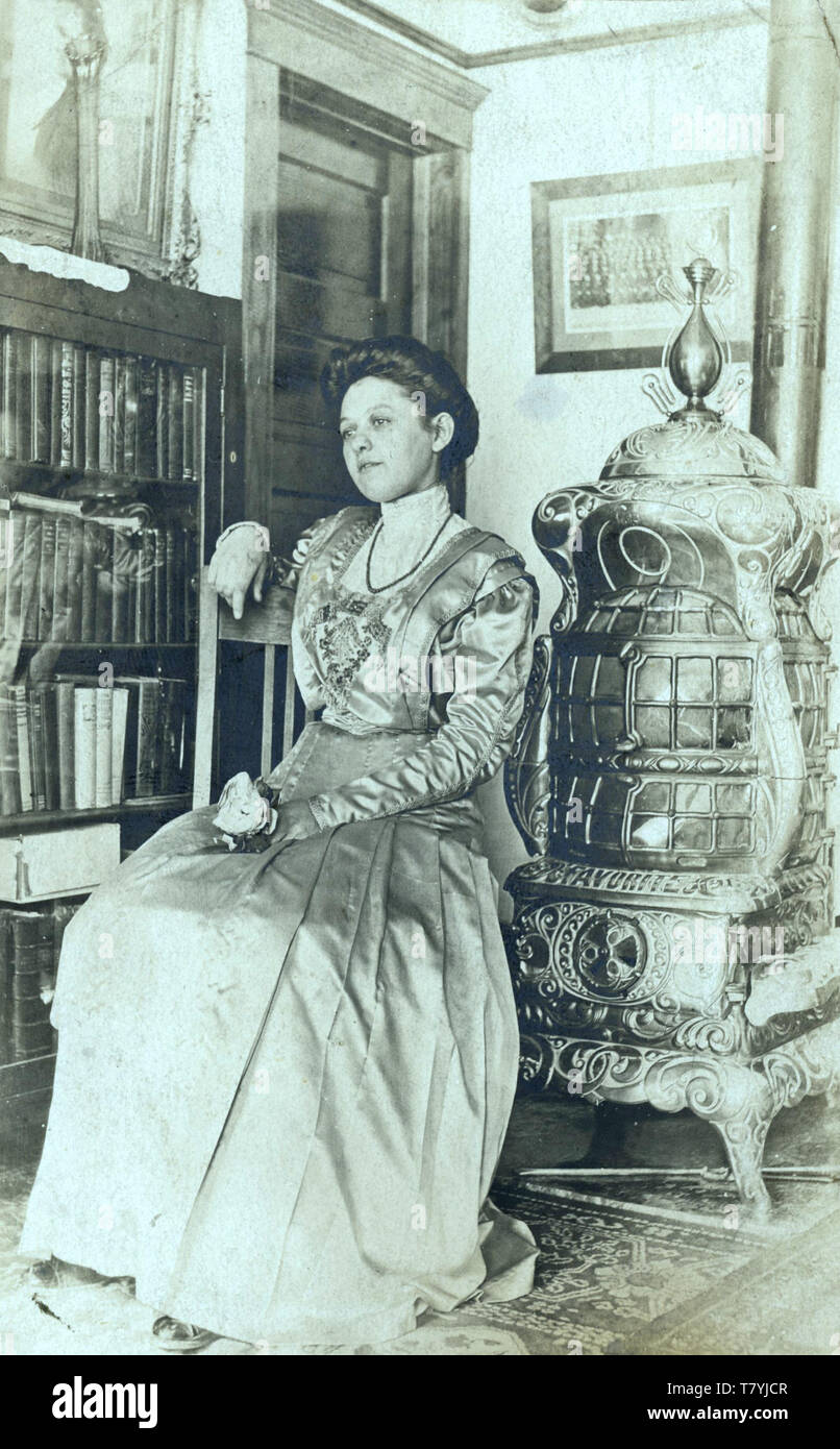 Woman in Victorian interior with cast iron room heater, ca. 1910.  New York State.  RPPC Stock Photo