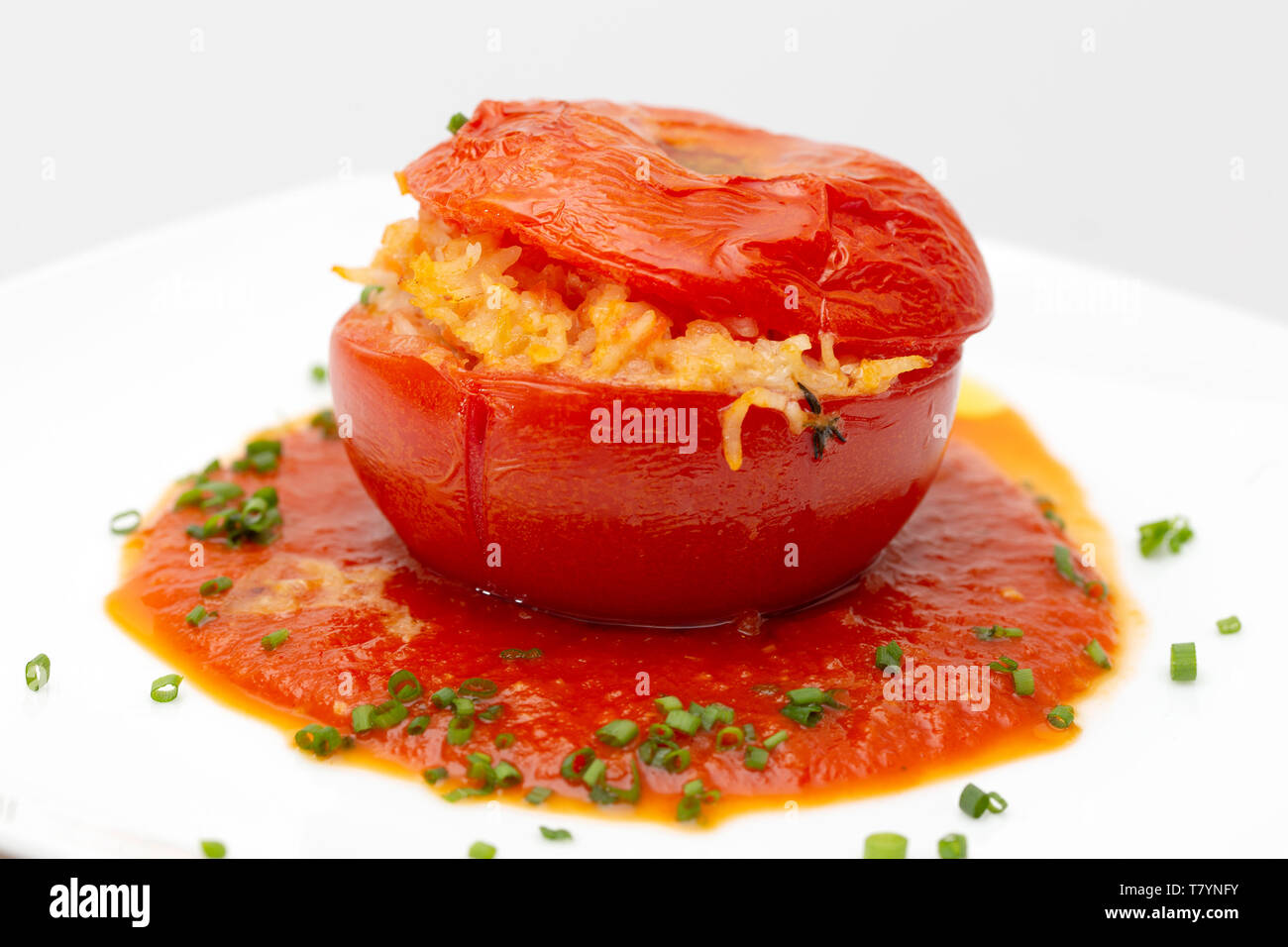 Side view of a tomato stuffed with rice and veg, served on a bed of sauce with a garnish of chopped chives. Stock Photo
