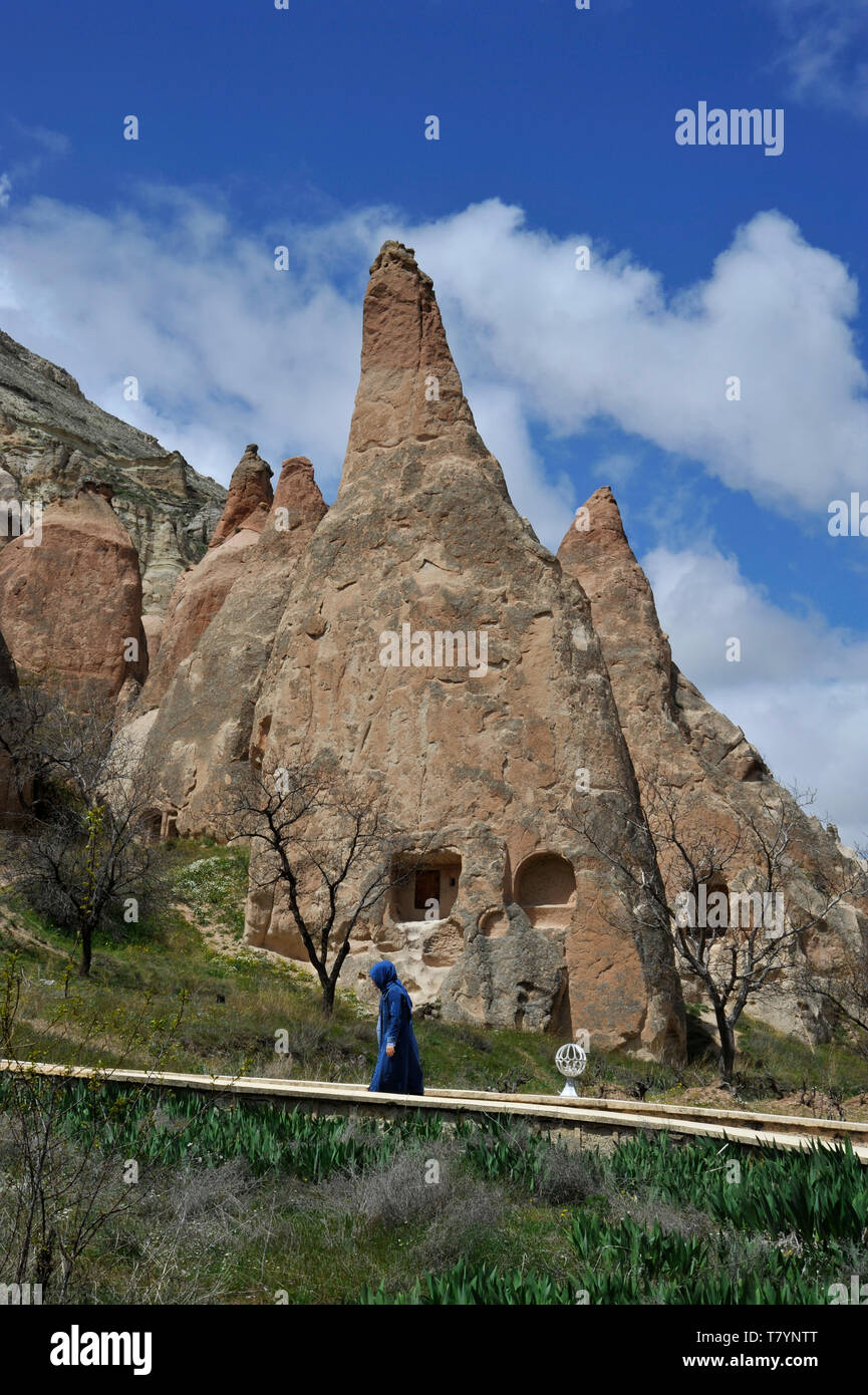 A Muslim woman walks along path through unusual rock formations at outdoor museum in Cappadocia, Turkey Stock Photo