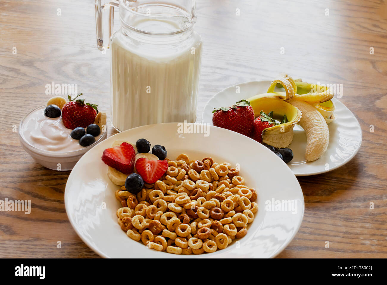 Bowl of oat cereal on a wooden table with yogurt, milk, strawberries, blueberries, and banana. Stock Photo