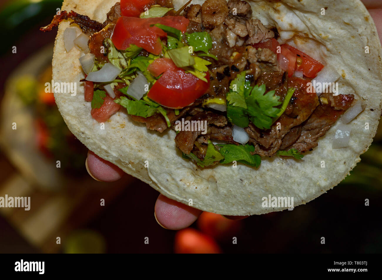 Mexican tacos, holding grilled carne asada taco with radishes, limes, spring onions, low key with copy space Stock Photo