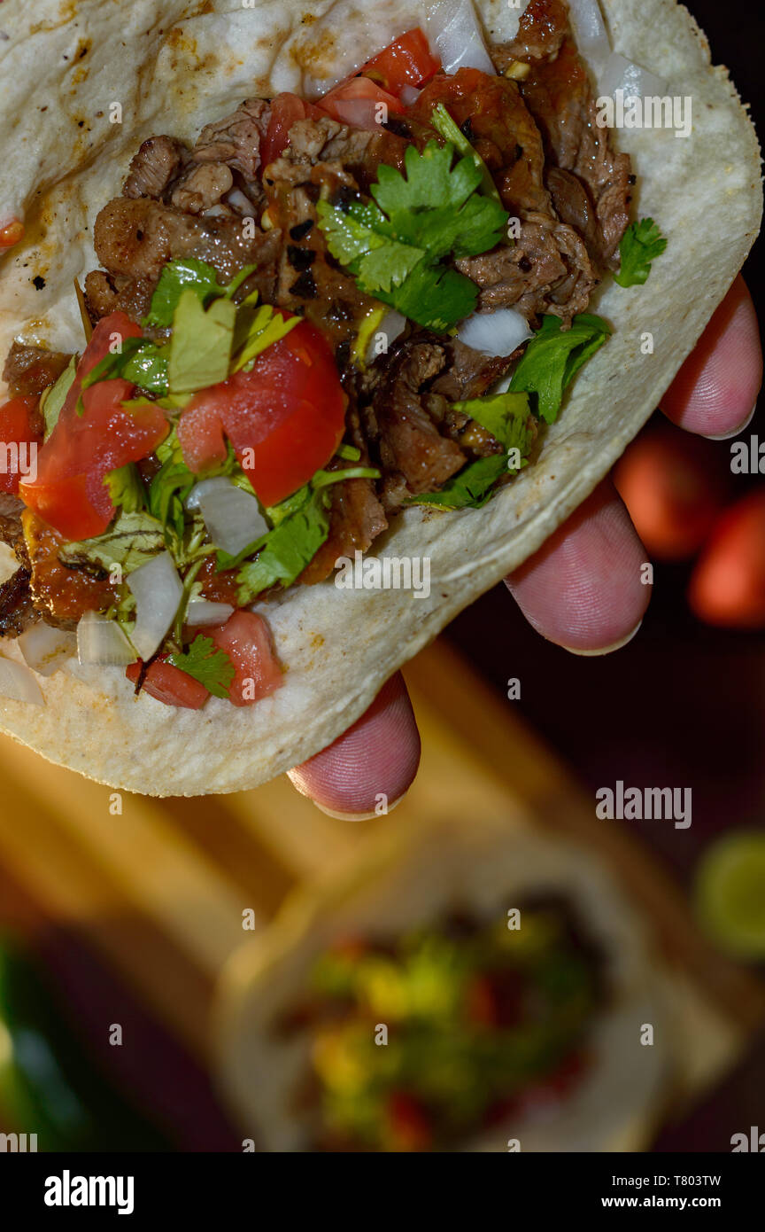 Tijuana tacos, holding grilled carne asada taco with radishes, limes, spring onions, low key with copy space Stock Photo
