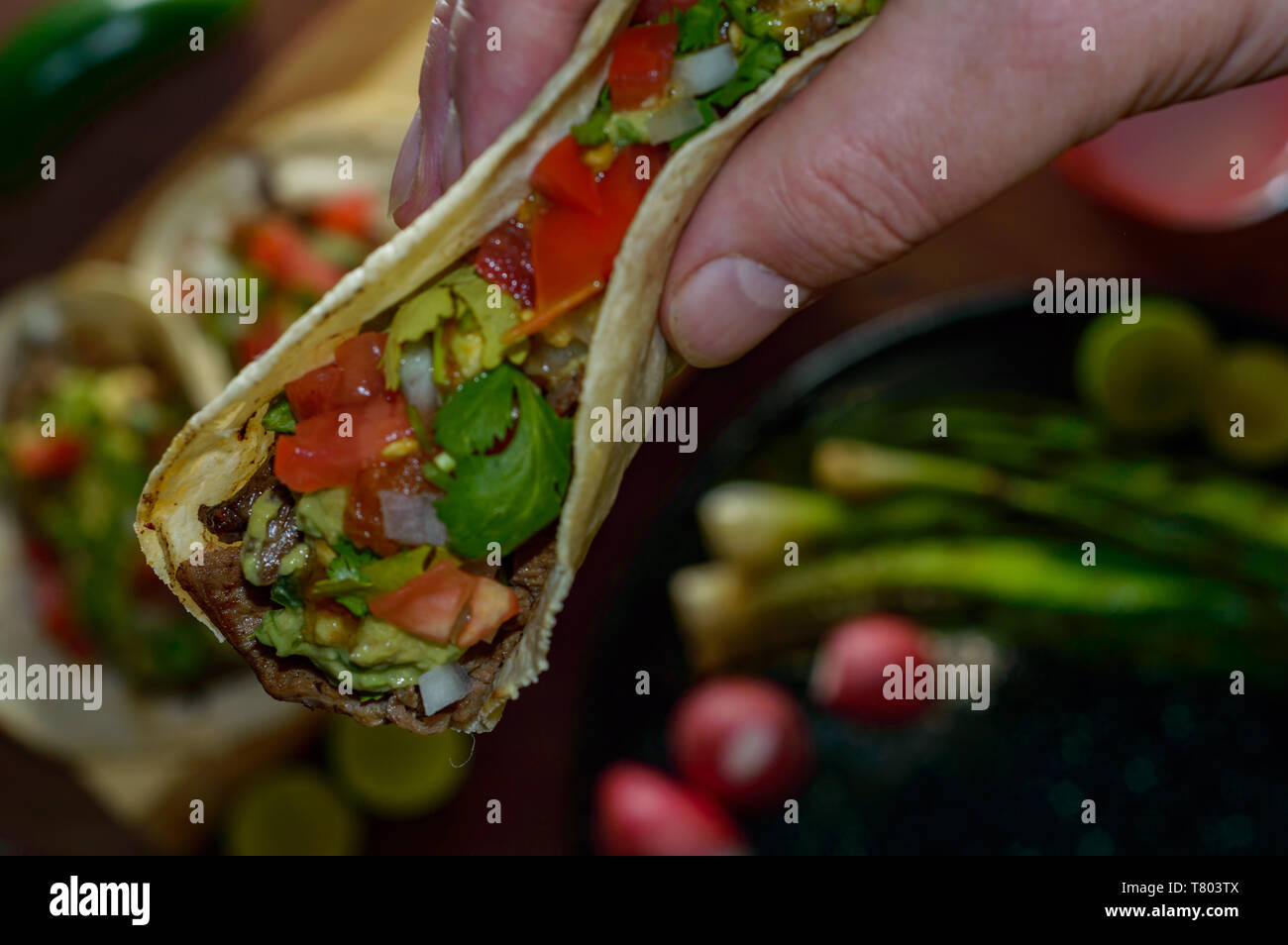 Tijuana tacos, lifting grilled carne asada with radishes, limes, spring onions, low key with copy space Stock Photo