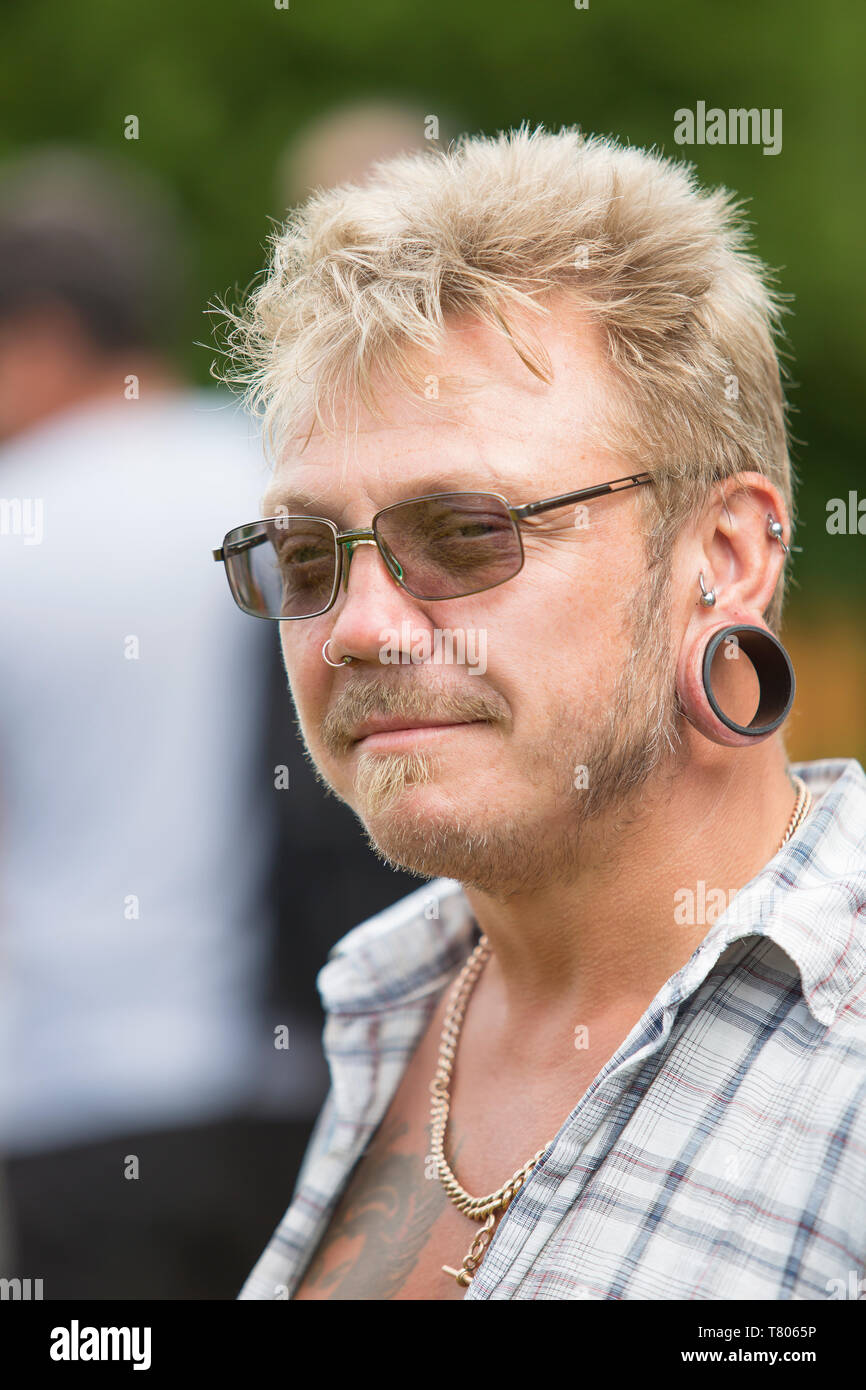 Close, front portrait of blonde-haired, caucasian male with stretched ear lobe piercings. UK man with ear lobes stretched in large round earrings. Stock Photo