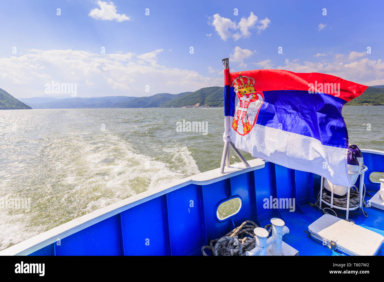 Serbia national flag on tourist boat , Danube river landscape and sky with clouds in background Stock Photo