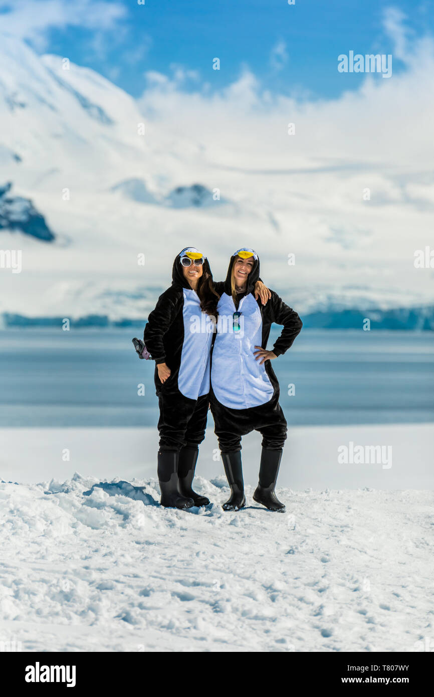 Two American women tourists in Penguin Onesies on sunny day, posing on the glaciers, Antarctica, Polar Regions Stock Photo