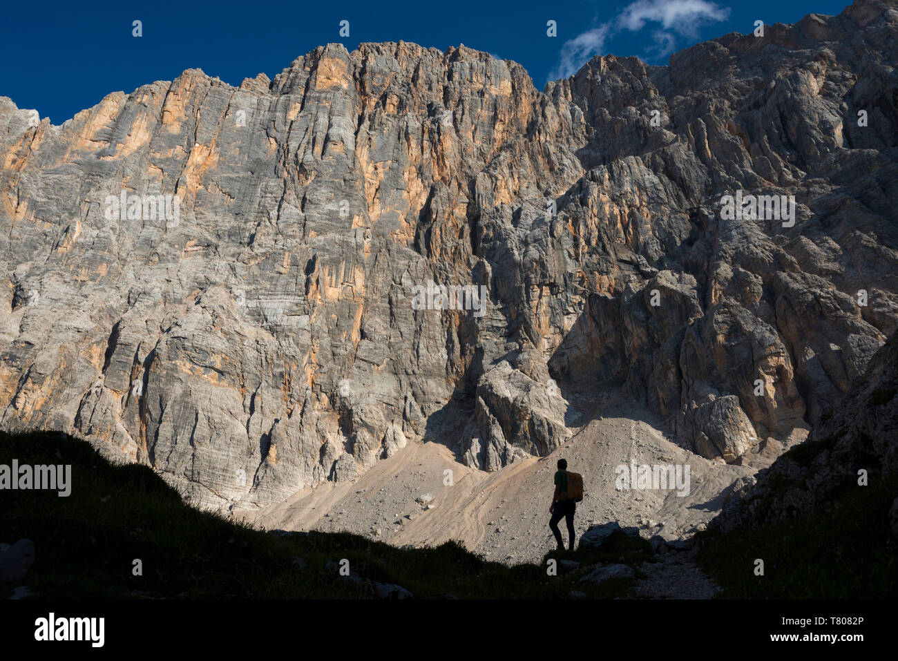 A trekker takes a break from the trail under the impressive northwest vertical wall of Monte Civetta in the Dolomites, Belluno, Veneto, Italy, Europe Stock Photo