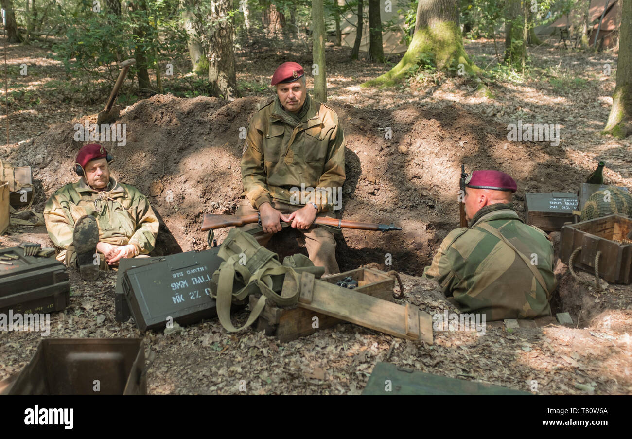 Woodhall Spa 1940s world war two festival re-enactment weekend. Three paratroopers sitting in a foxhole surrounded by woodland, and ammunition boxes Stock Photo