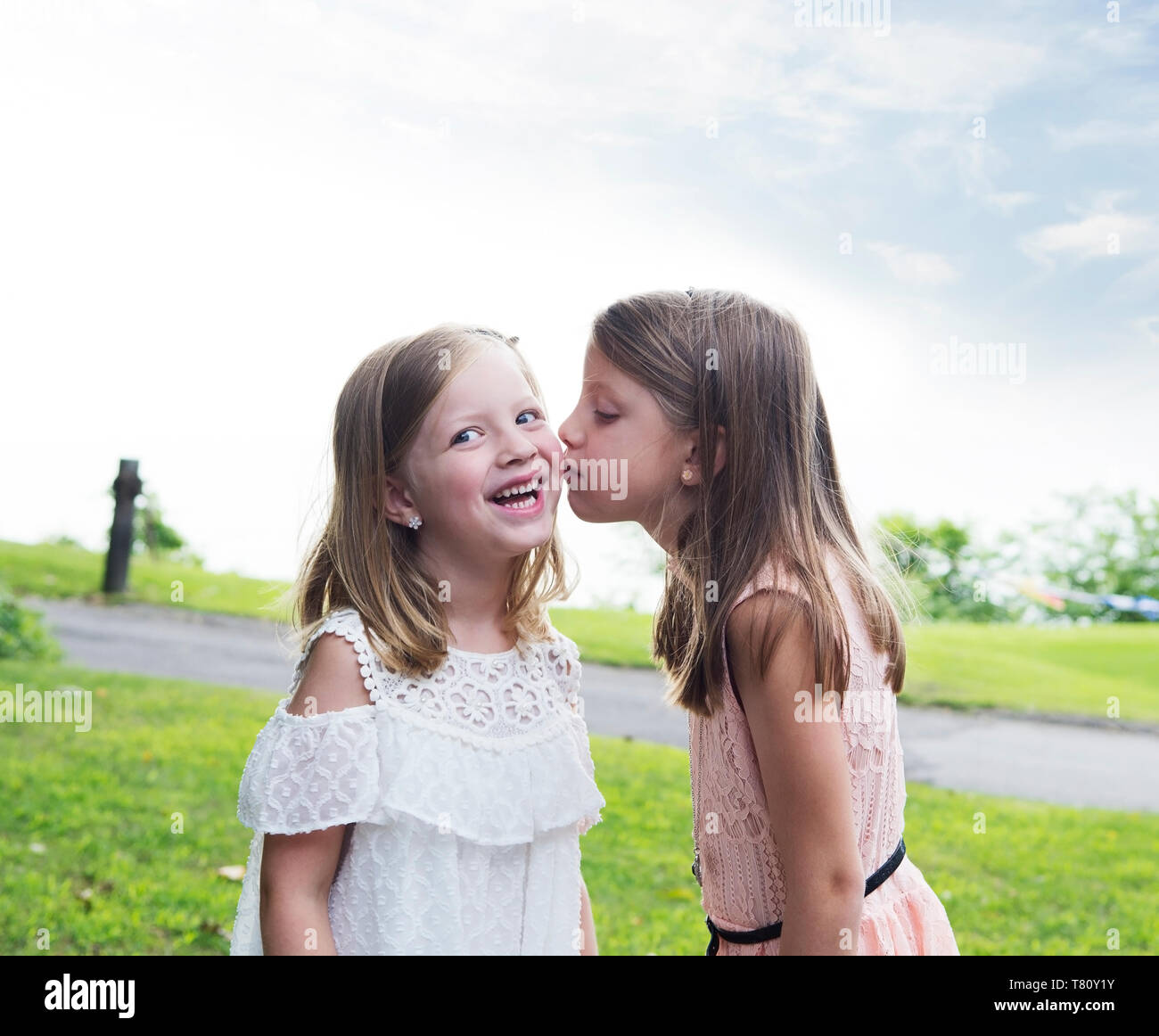 Two sisters, young children kissing in a park during summer Stock Photo