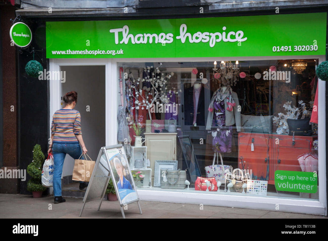 A woman entering a Thames Hospice charity shop in Henley-on-Thames carrying two bags of donations Stock Photo