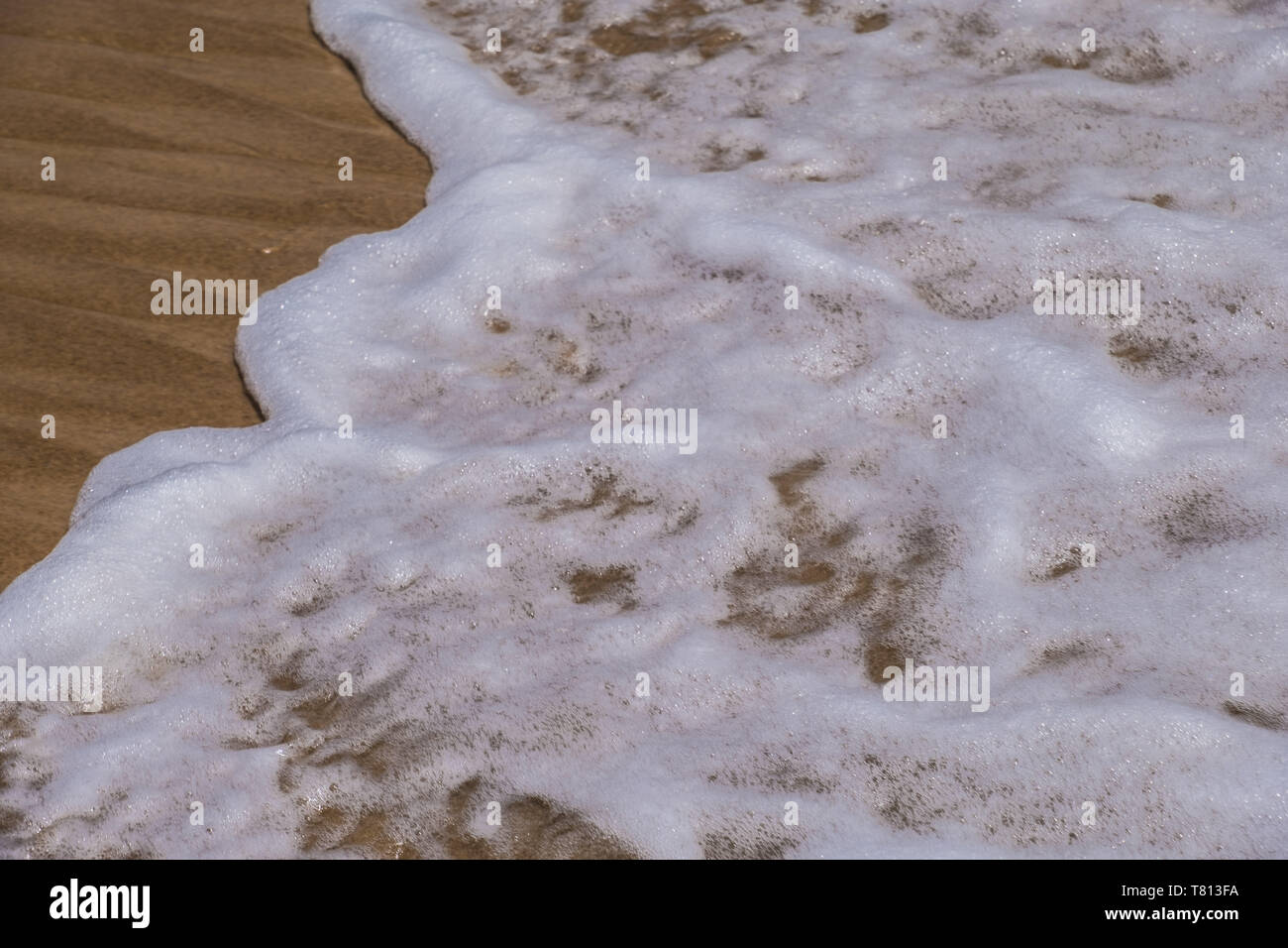 Sea or oceanic wave washing over sand - foamy pattern, background. Photo of wet sand on the beach. Stock Photo