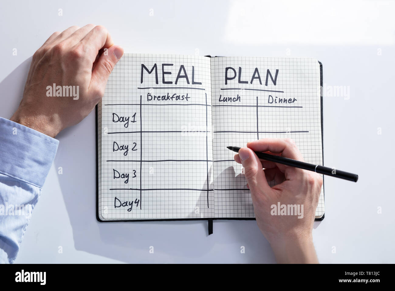 High Angle View Of A Person Hand Filling Meal Plan In Notebook At Desk Stock Photo
